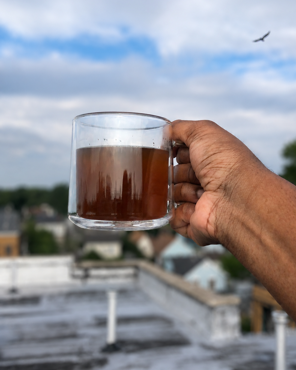 Hand holding a glass mug of hot beverage on a rooftop with a blurred background